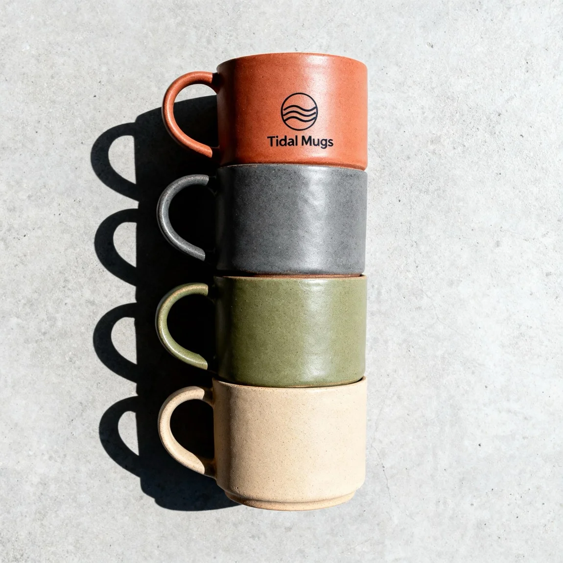 An organized top-down flat lay showcases a stack of four handmade mugs in complementary earthy tones. | ai product photo